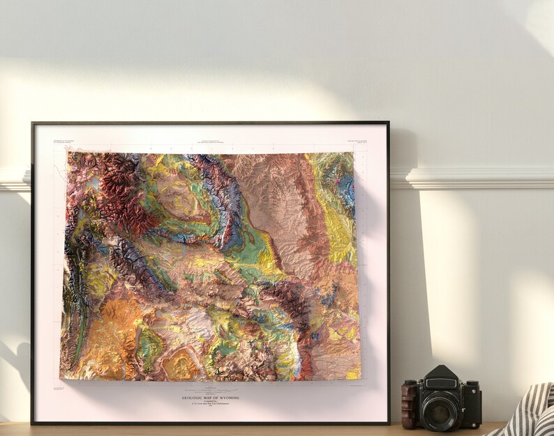Puede incluir: Un mapa geol&oacute;gico enmarcado de Wyoming con un dise&ntilde;o colorido, texturizado y con un aspecto 3D. El mapa muestra las diferentes formaciones rocosas y caracter&iacute;sticas geol&oacute;gicas del estado.