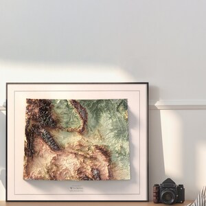 May include: A framed topographic map of Wyoming with a brown, green, and beige color scheme. The map is in a black frame with a white mat.