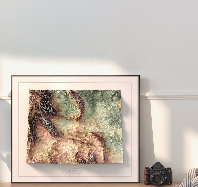 May include: A framed topographic map of Wyoming with a brown, green, and beige color scheme. The map is in a black frame with a white mat.