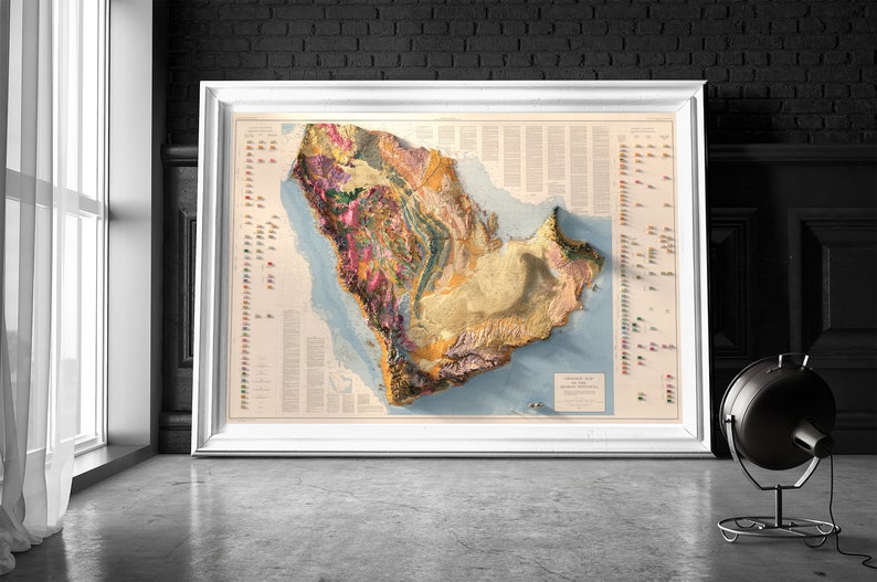 May include: A detailed, colourful, 3D relief map of Saudi Arabia, framed in white, with a legend and key on the right side. The map shows the geological formations and features of the country.