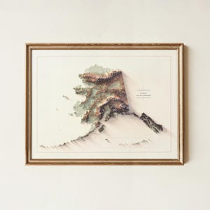 May include: Framed elevation map of Alaska, featuring a 3D topographic representation in shades of brown, green, and white. The map is set against a cream-colored background and enclosed in a gold-colored frame. The text "Elevation Map Alaska" is visible.