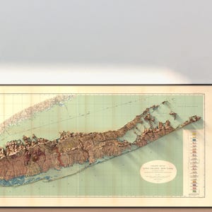 May include: A vintage, detailed relief map of Long Island, New York, printed on paper with a green background and brown relief features. The map is framed in a black frame and includes a legend with colored flags.