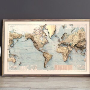 May include: A framed world map print featuring a three-dimensional relief effect with gold-toned landmasses against a pale blue ocean background. The map displays detailed topography and includes small text blocks and circular diagrams in the corners.