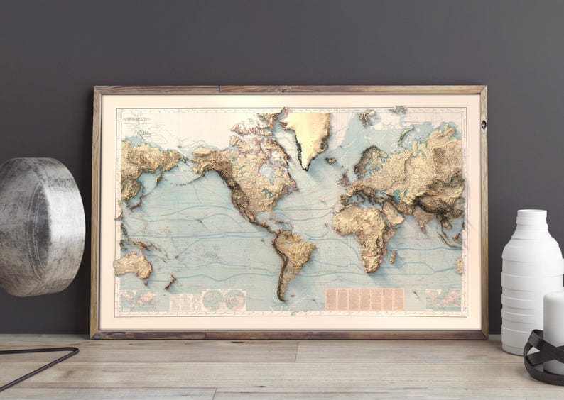 May include: A framed world map print featuring a three-dimensional relief effect with gold-toned landmasses against a pale blue ocean background. The map displays detailed topography and includes small text blocks and circular diagrams in the corners.