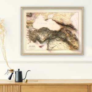 May include: A vintage map of Asia Minor, also known as Anatolia, with a 3D relief effect. The map shows the Black Sea, the Mediterranean Sea, and the Aegean Sea. The map is framed in a gold-colored frame.
