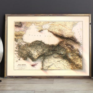 May include: A vintage map of Asia Minor, showing the topography of the region with detailed lines and shading. The map is framed in a wooden frame and has a light beige background.