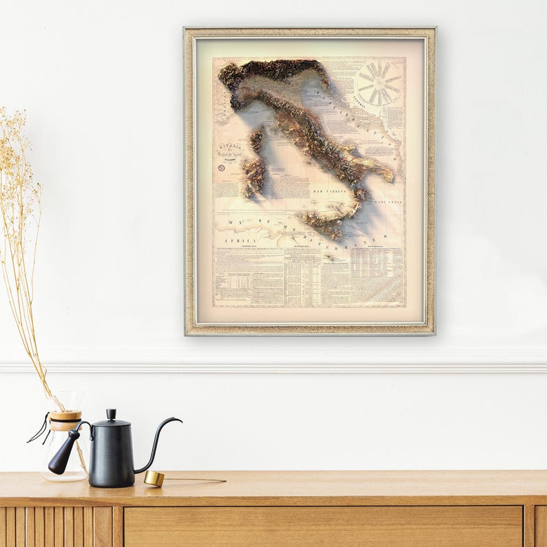 May include: A framed vintage map of Italy with a 3D embossed effect. The map is printed on a cream-colored paper with brown and beige details. The map is surrounded by a thin, gold-colored frame.