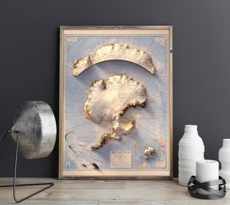 May include: A vintage-style map of Antarctica in a wooden frame. The map is printed on a light blue background with brown lines and text. The continent of Antarctica is shown in a light brown colour with a 3D effect.