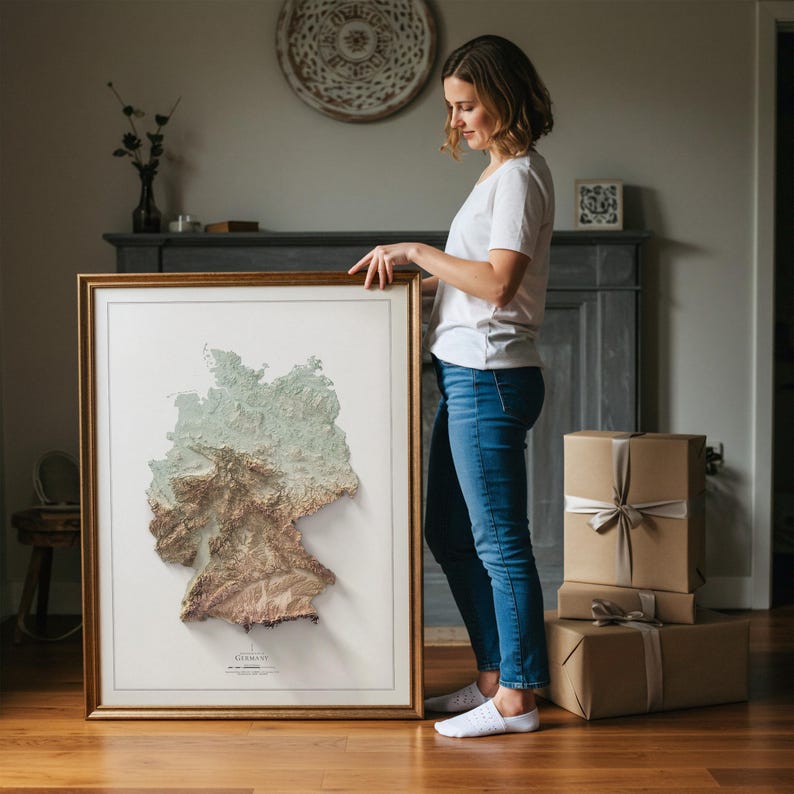 May include: A framed 3D map of Germany, depicting the country's topography in green, brown, and beige tones. The map is set within a gold-coloured frame. The map is a unique piece of home decor.