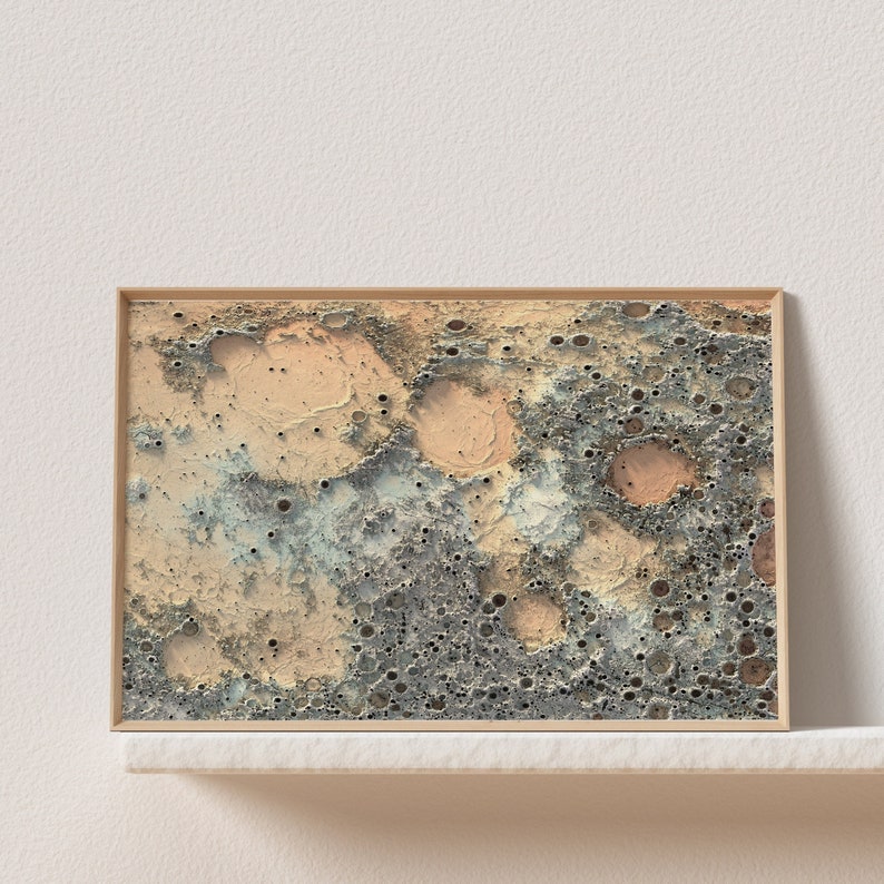May include: A framed abstract print with a textured, cratered surface in shades of beige, gray, and blue. The print has a modern, minimalist aesthetic.