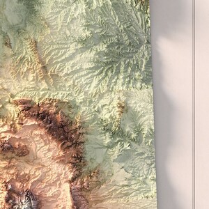 May include: A close-up of a topographic map showing a mountainous region with shades of green, brown, and beige.