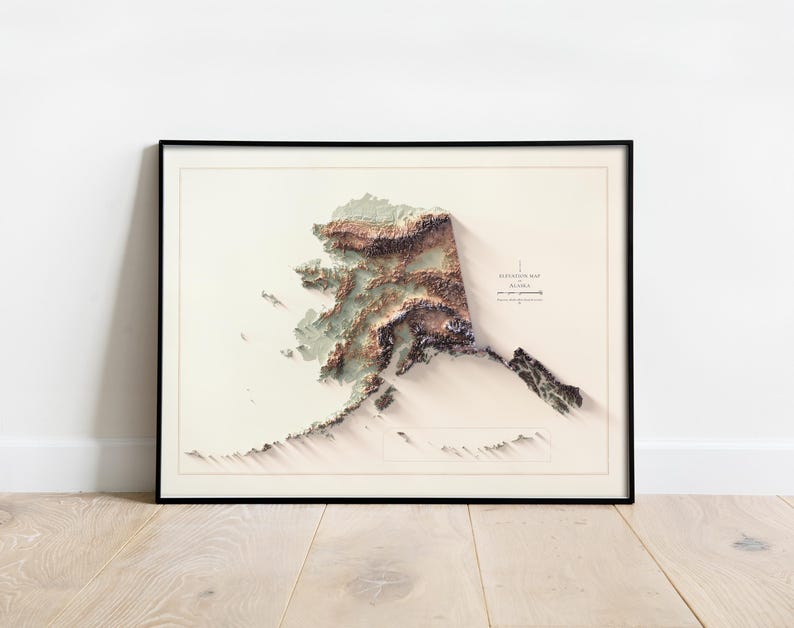 May include: Framed elevation map of Alaska, featuring a 3D topographic representation in shades of brown, green, and white. The map is set against a cream-colored background, enclosed in a black frame. The text "ELEVATION MAP ALASKA" is visible.