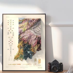 Op de afbeelding: Een vintage-stijl geologische kaart van Indiana, die de diverse rotsformaties van de staat laat zien in een kleurrijke, 3D-reli&euml;fstijl. De kaart is ingelijst in zwart en wordt getoond op een witte muur.