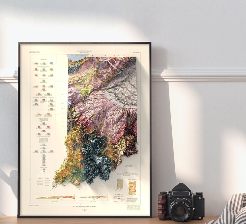 Op de afbeelding: Een vintage-stijl geologische kaart van Indiana, die de diverse rotsformaties van de staat laat zien in een kleurrijke, 3D-reli&euml;fstijl. De kaart is ingelijst in zwart en wordt getoond op een witte muur.