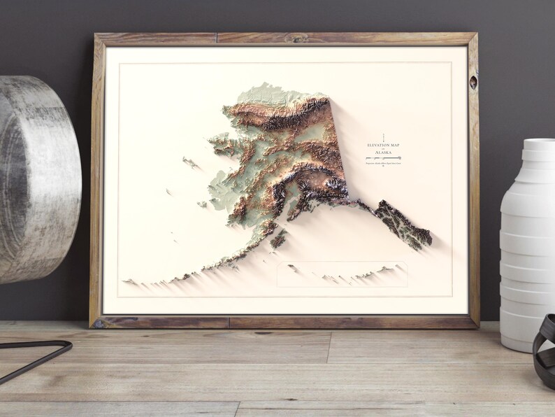 May include: A framed 3D relief map of Alaska, showcasing the state's topography in shades of brown, green, and white. The map is set against a white background within a wooden frame. The text "Elevation Map Alaska" is visible.