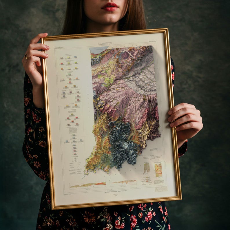 May include: Framed map of Indiana in a gold-coloured frame. The map displays a detailed, multi-coloured relief, showing the state's topography. The map is held against a dark background.
