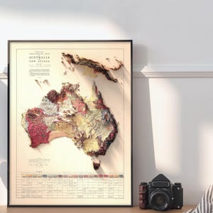 May include: A vintage geological map of Australia and New Guinea, printed in black and white with colored geological formations. The map is framed in a black frame and is hanging on a white wall.