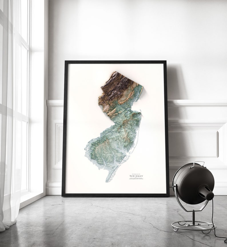 May include: A framed print of a topographic map of New Jersey. The map is in shades of green, brown, and white, and shows the state's terrain in detail. The print is framed in a black frame and is hanging on a white wall.