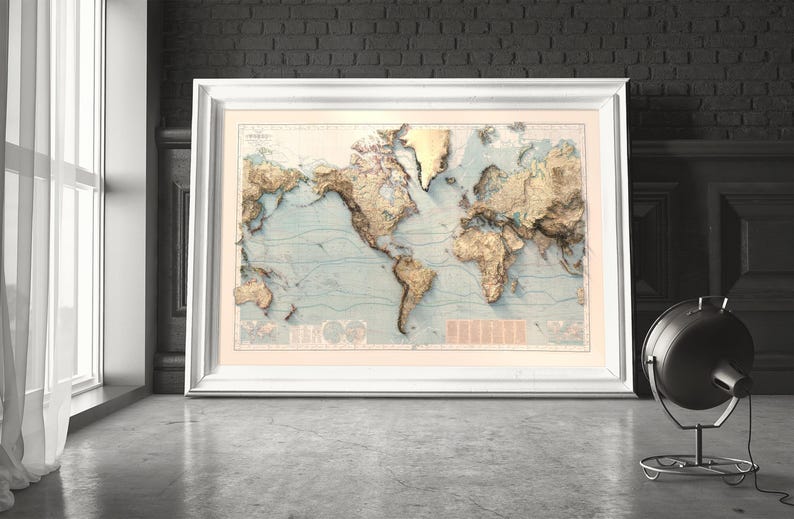 May include: A large, framed world map print featuring a relief-style design with raised-looking golden landmasses set against a pale blue ocean background. The map includes detailed topographical shading, thin contour lines, and a white frame.