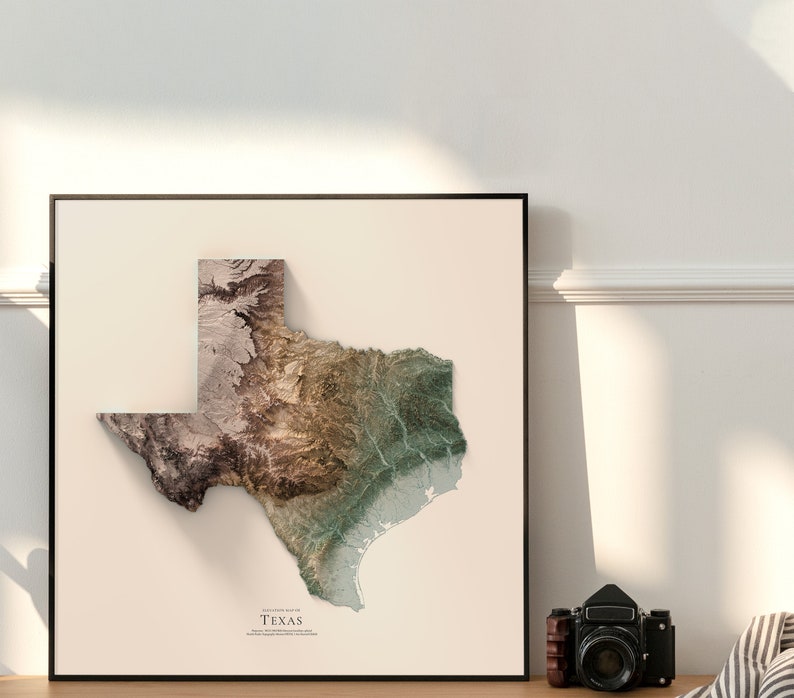 Może przedstawiać: Wydruk topograficznej mapy Teksasu w ramie. Mapa jest w odcieniach brązu, zieleni i beżu, na białym tle. Tekst "Texas" jest nadrukowany na dole pośrodku mapy.