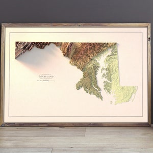 May include: A framed 3D topographic map of Maryland with a beige background. The map is in shades of brown, green, and yellow, showing the state's terrain.
