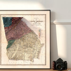 May include: A vintage map of the State of Georgia, showing geological features. The map is printed in black and white with colored lines and text. The map is framed in a black frame.