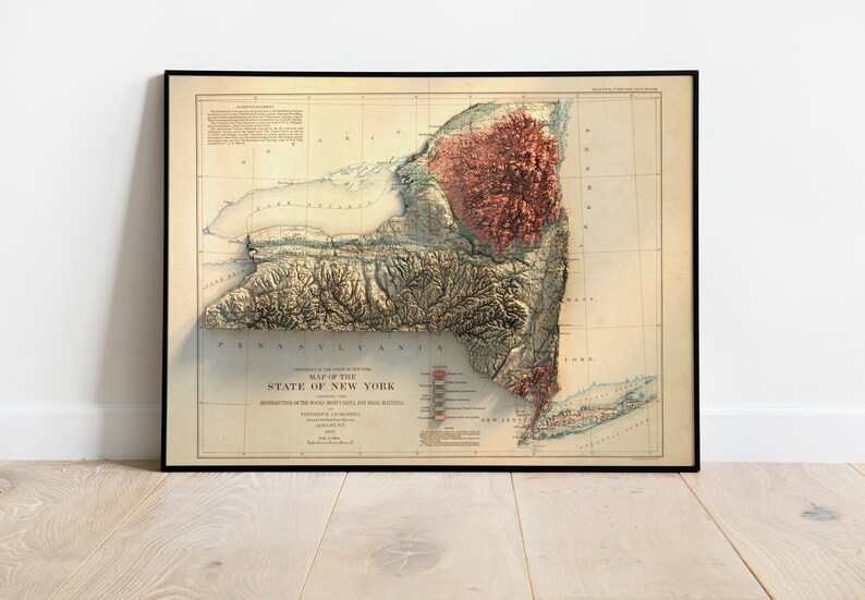 May include: Framed vintage map of New York State, featuring a 3D relief of the terrain. The map is in a black frame and has a beige background with detailed geographical features and text. The title reads "Map of the State of New York."