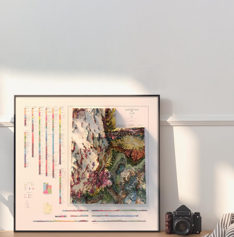 May include: A framed topographic map of Utah with a 3D relief effect. The map is printed on a cream-colored background with a legend and scale bar. The map is framed in black.