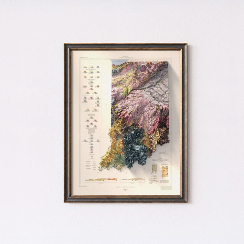 May include: Framed 3D topographic map of Indiana, showing detailed relief of the state's terrain. The map uses a vibrant colour palette with shades of green, yellow, purple, and blue. The map is encased in a dark wooden frame.