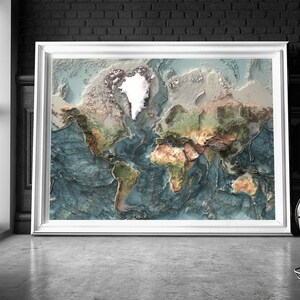 May include: A framed world map with a 3D effect, showing the continents in various shades of green, brown, and beige, with the oceans in shades of blue. The map is framed in white and is hanging on a brick wall.