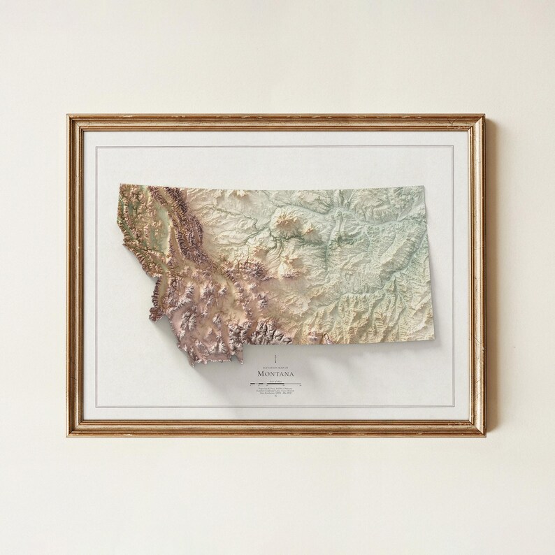 May include: Framed 3D relief map of Montana, showcasing the state's topography in shades of brown, green, and beige. The map is set within a gold-colored frame, offering a detailed representation of the state's landscape.