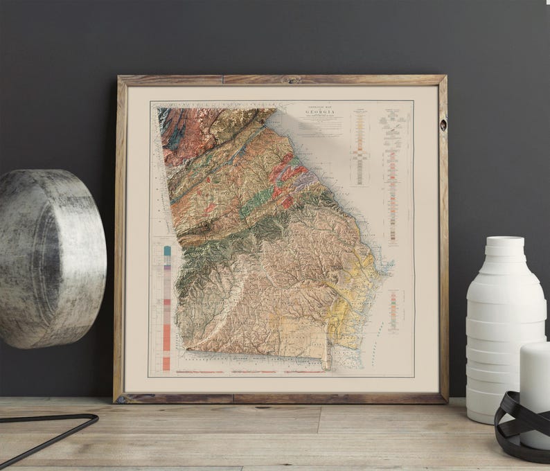 May include: A vintage map of Georgia with a detailed topographic relief showing the state's physical features. The map is printed in shades of brown, green, and blue, with a color key on the right side. The map is framed in a simple wooden frame.