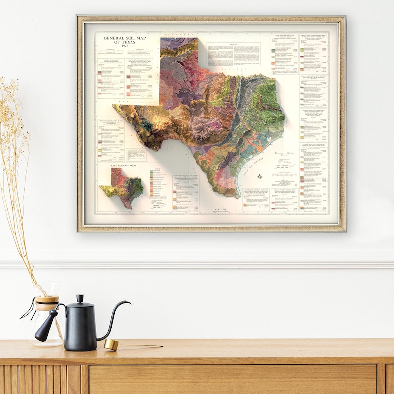 May include: A vintage map of Texas showing the general soil map of the state. The map is framed in a light wood frame and has a white background. The map is in a 3D style, with the state of Texas raised from the surface. The map is labeled "General Soil Map of Texas 1923".