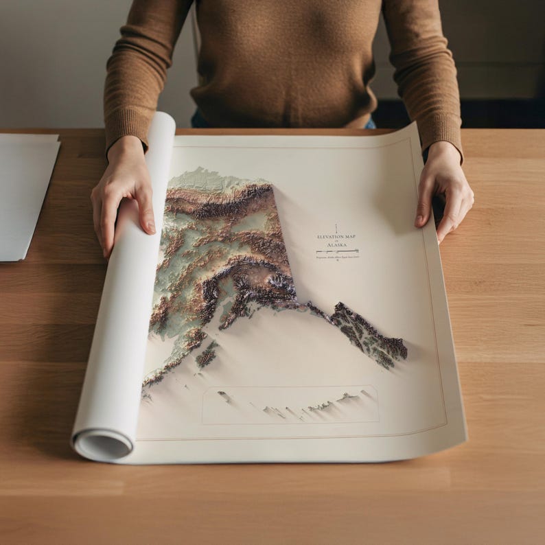 May include: A rolled-up map of Alaska, featuring a 3D elevation design in shades of brown, green, and white. The map is being unrolled on a wooden surface. The map includes the text "Elevation Map Alaska".