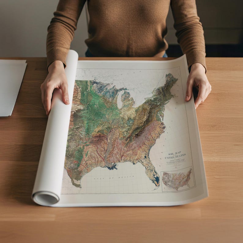May include: A rolled-up white map of the United States is being unrolled on a wooden table. The map features a detailed topographical design with various colors representing different elevations. The map is labeled "MID MAP UNITED STATES".