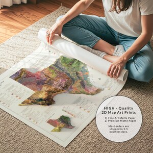 Op de afbeelding: Een persoon zit op een kleed en rolt een grote kaartkunstprint uit. De kaart heeft een 3D topografisch ontwerp met verschillende kleuren. De print bevat de tekst "HIGH - Quality 2D Map Art Prints". De kaart is gedrukt op mat papier.