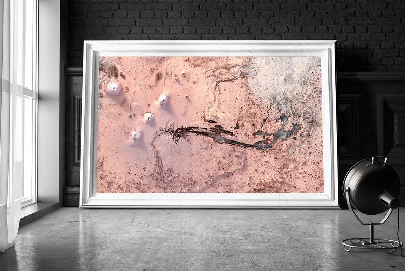 May include: An aerial photograph of a pink and white landscape with a winding black line through the centre. The landscape is covered in small, white mounds.