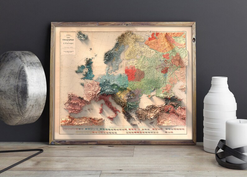 Op de afbeelding: Een vintage-stijl kaart van Europa met een 3D-effect, die verschillende regio's in verschillende kleuren laat zien. De kaart is ingelijst in een houten lijst en heeft een titel in het Frans: "Carte Oro-Hydrographique de L'Europe".