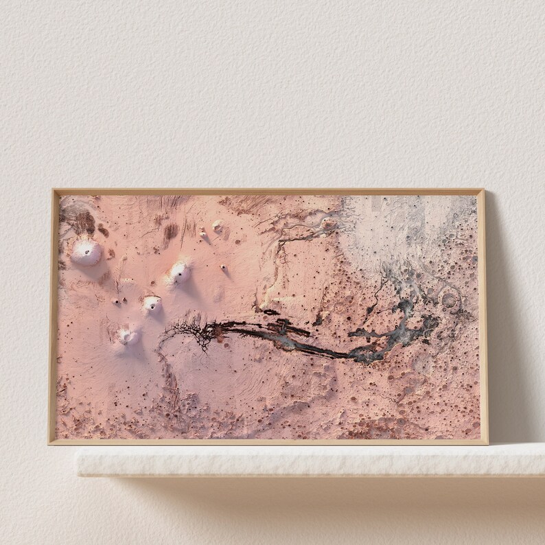 May include: A framed abstract art print with a pink and white background. The print features a dark grey line that resembles a river winding through the landscape. There are several white circular shapes scattered throughout the print.