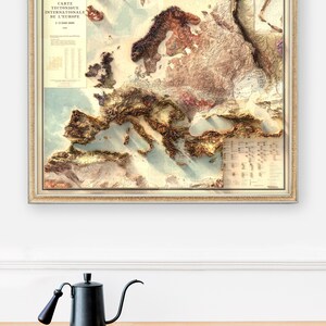 Pu&ograve; includere: Una mappa vintage incorniciata dell'Europa con un dettagliato rilievo topografico che mostra le montagne e le valli. La mappa &egrave; intitolata "Carte Tectonique Internationale de L'Europe 1:2 500 000".