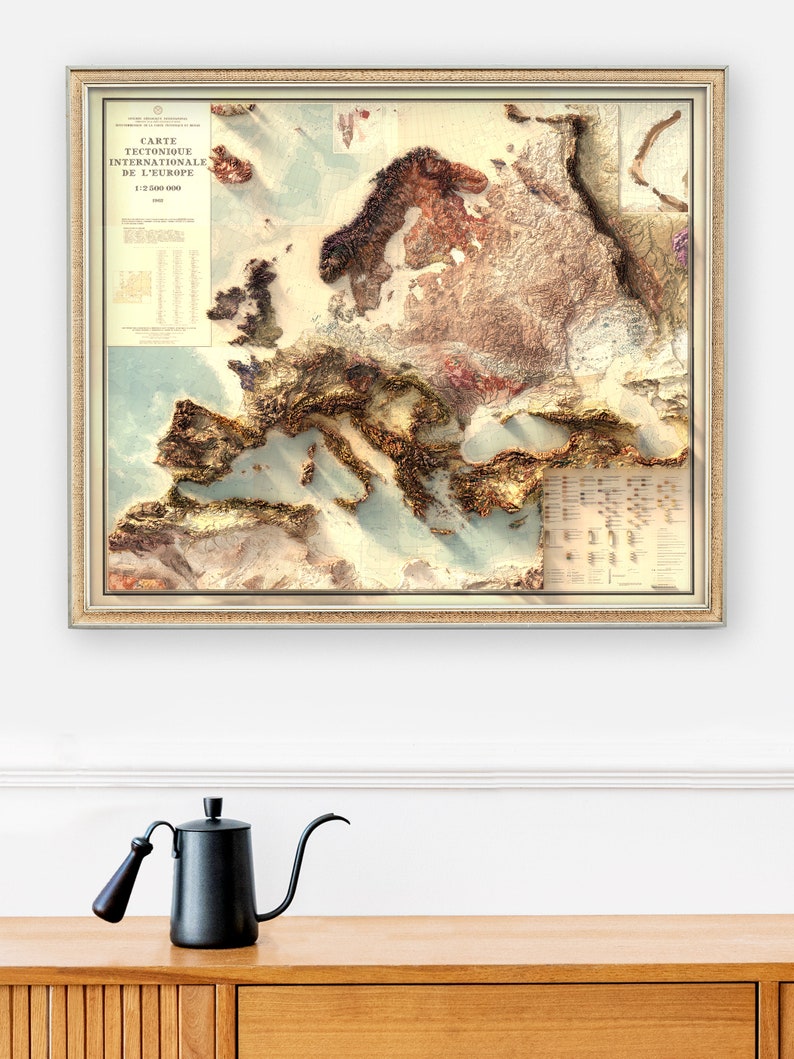 Pu&ograve; includere: Una mappa vintage incorniciata dell'Europa con un dettagliato rilievo topografico che mostra le montagne e le valli. La mappa &egrave; intitolata "Carte Tectonique Internationale de L'Europe 1:2 500 000".