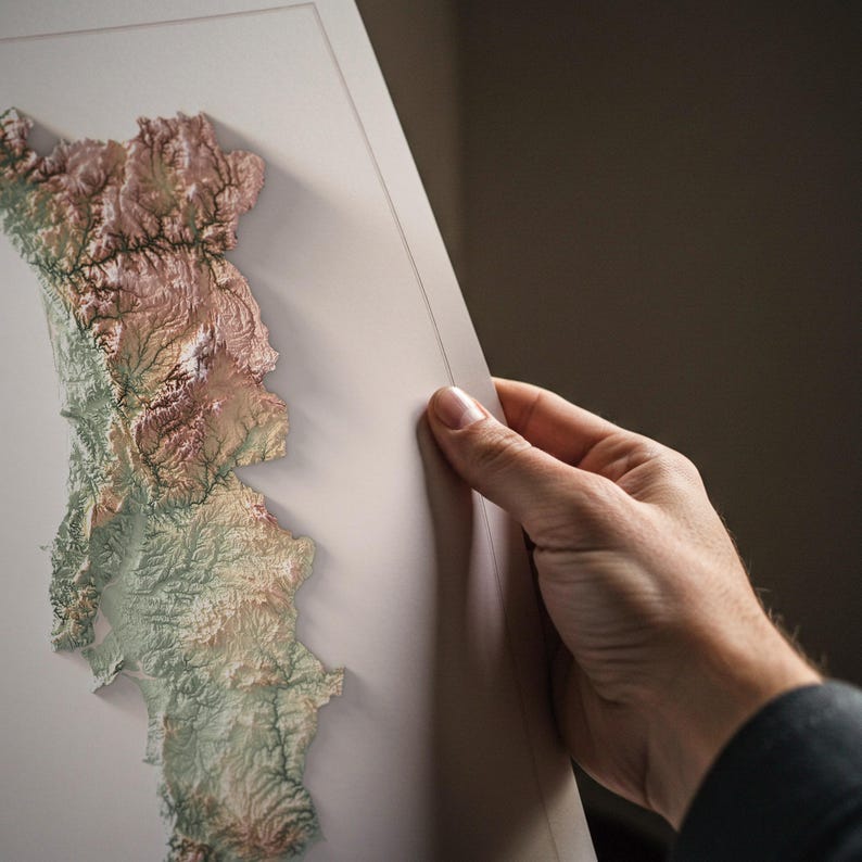 May include: A detailed, three-dimensional relief map of a landmass, showcasing varying elevations with a palette of earthy tones. The map is held by a hand, revealing its intricate topographical features and textures.