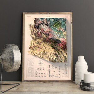 May include: A vintage-style topographic map of Arizona in a wooden frame. The map is printed on a cream-colored paper with a detailed relief map of the state in shades of green, brown, and pink. The map includes a legend and a scale bar.