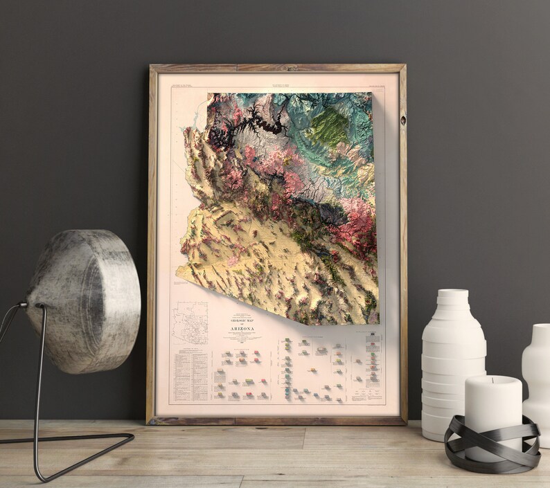 May include: A vintage-style topographic map of Arizona in a wooden frame. The map is printed on a cream-colored paper with a detailed relief map of the state in shades of green, brown, and pink. The map includes a legend and a scale bar.