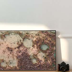May include: A framed abstract art print with a textured, mottled surface in shades of brown, beige, and green. The print resembles a close-up of the moon's surface.