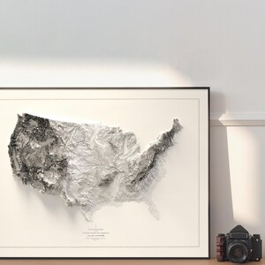 Pu&ograve; includere: Una mappa in rilievo in bianco e nero degli Stati Uniti d'America, incorniciata da una cornice nera. La mappa mostra la topografia del paese, con montagne, valli e fiumi.