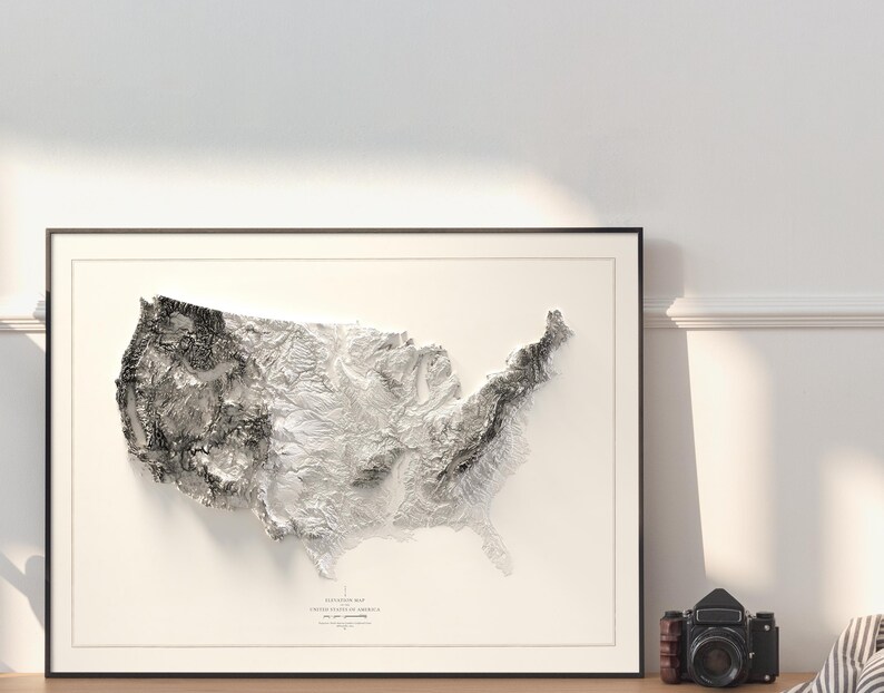 Pu&ograve; includere: Una mappa in rilievo in bianco e nero degli Stati Uniti d'America, incorniciata da una cornice nera. La mappa mostra la topografia del paese, con montagne, valli e fiumi.