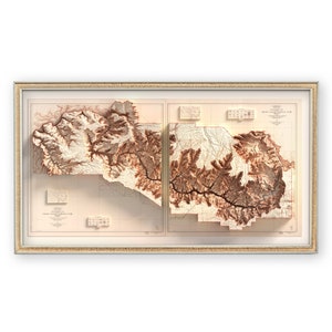 May include: Framed relief map of Grand Canyon National Park, showcasing the canyon's topography in shades of brown and beige. The map is encased in a light-colored wooden frame, offering a detailed 3D representation of the landscape.