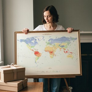 May include: A large rectangular world climate map framed in a thin gold-toned metal border. The map features a light cream background with various continents color-coded in shades of blue, green, yellow, orange, and red to represent climate zones.