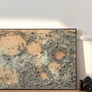 May include: A framed abstract print of a beige and gray textured surface with a pattern of craters. The print is in a black frame.